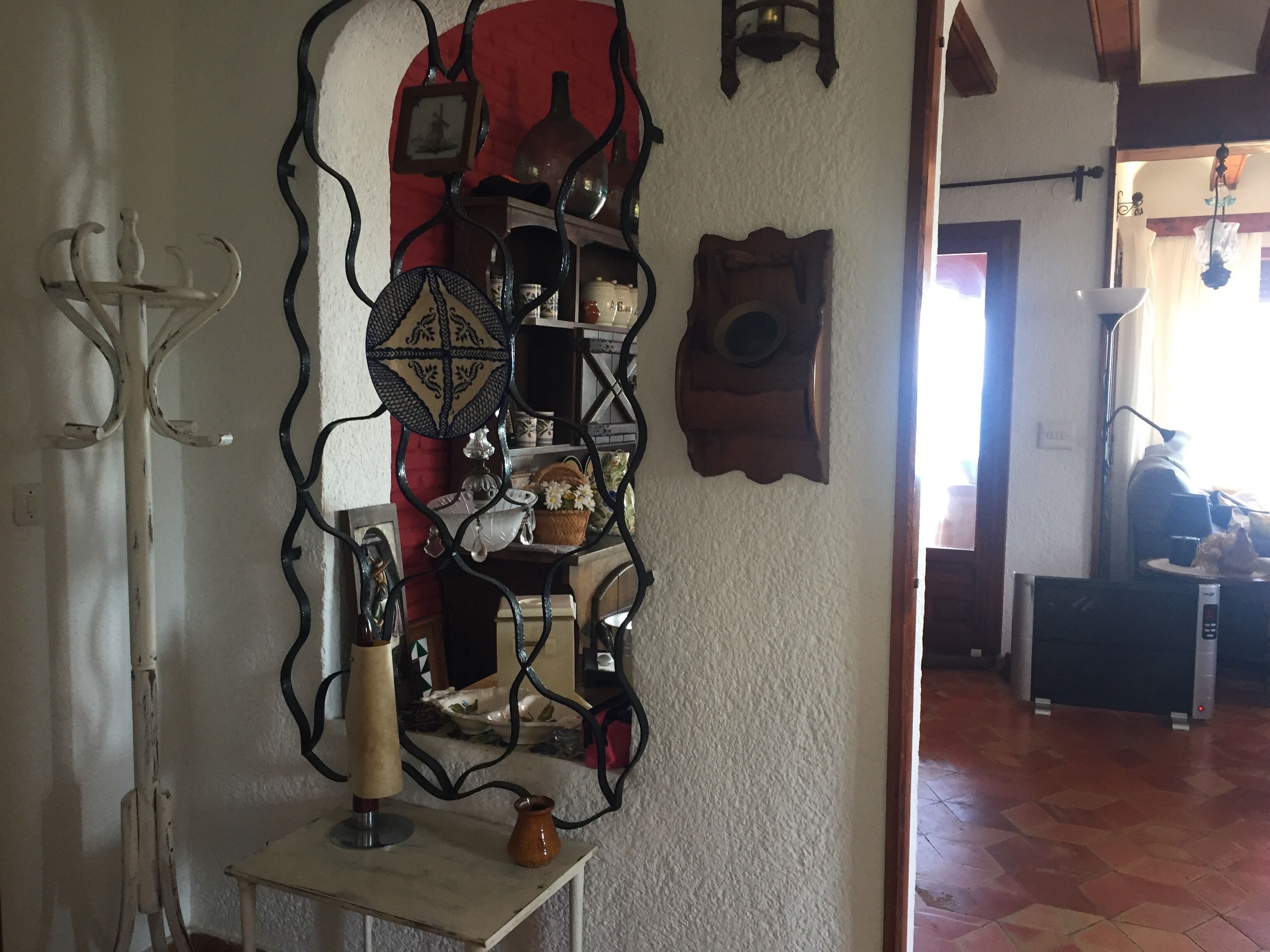 A room with a white wall, a wooden floor, and a decorative metal shelf with various items.