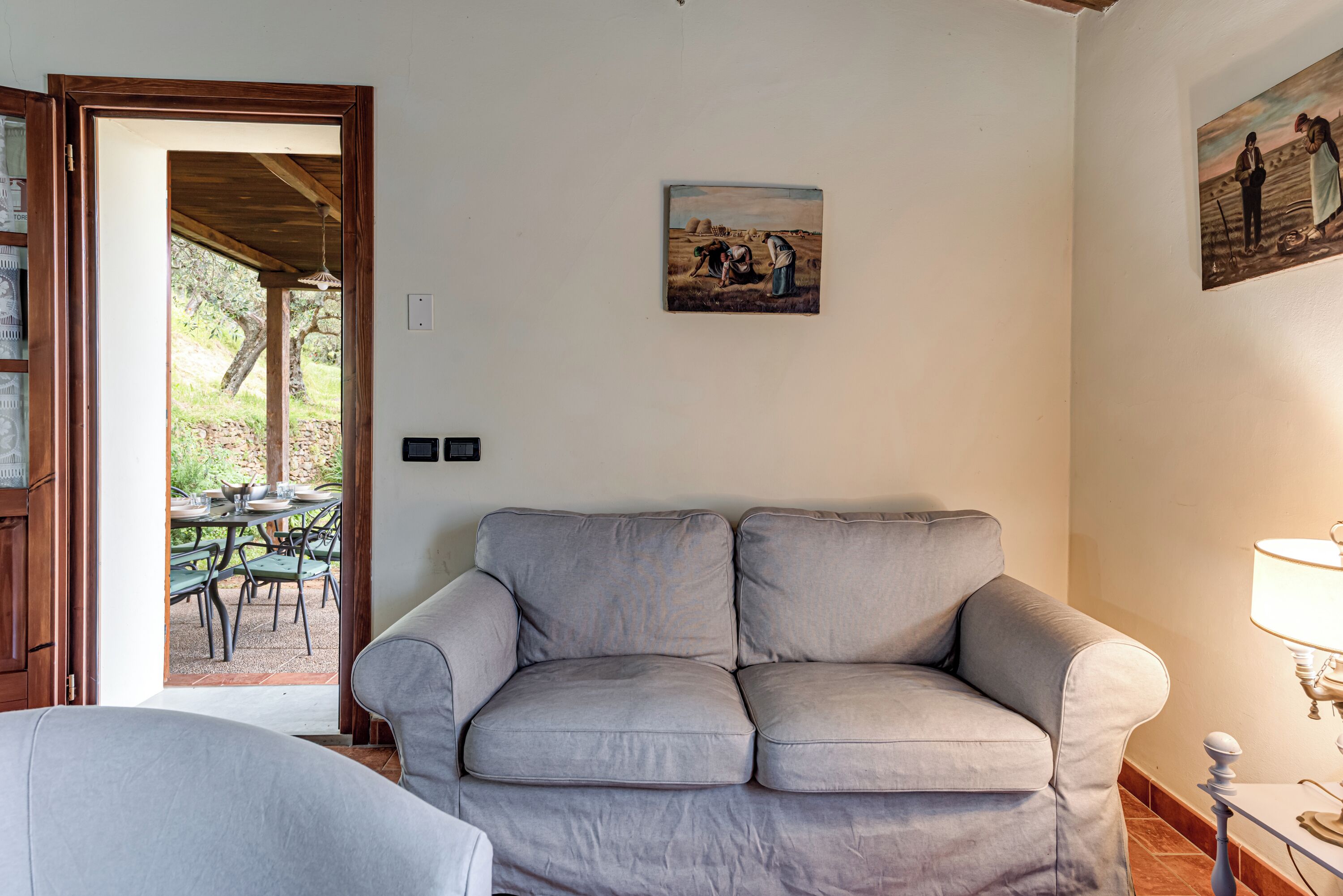 Een woonkamer met een grijze bank, een eettafel met stoelen en twee schilderijen aan de muur.
