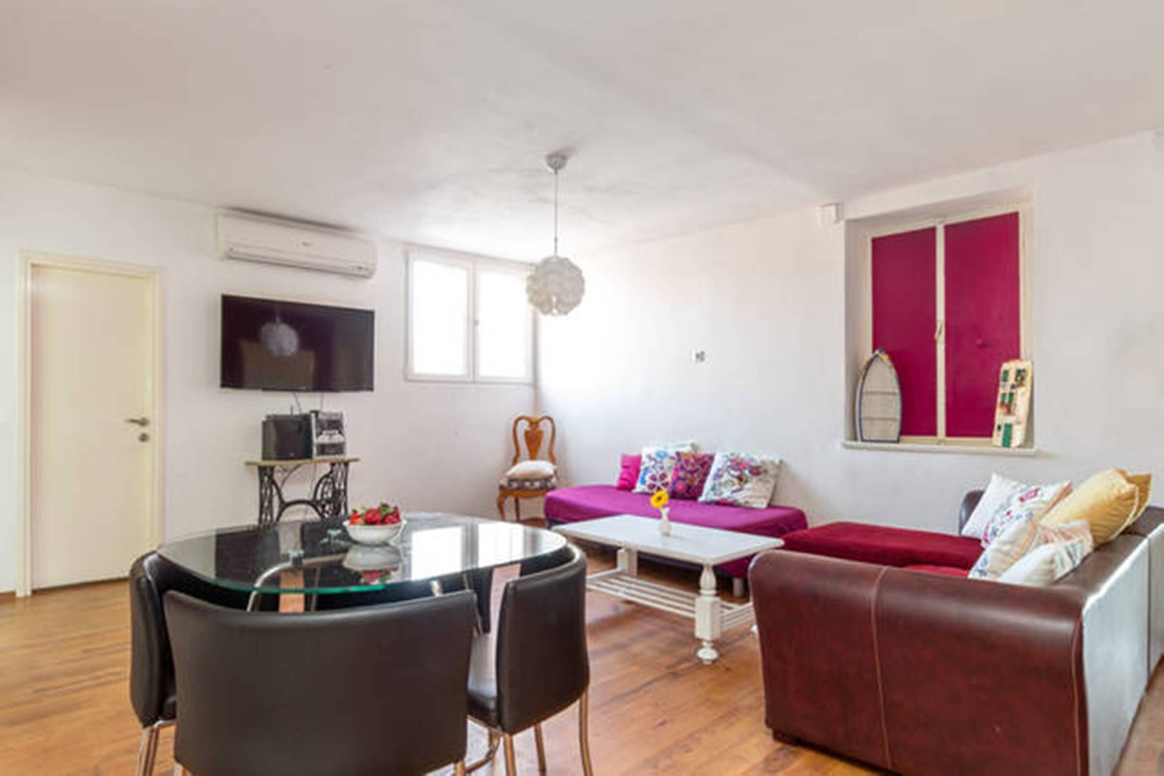 A living room with a red sofa, a glass coffee table, and a TV mounted on the wall.