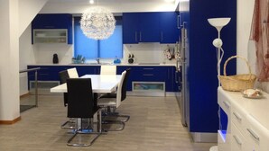 Une cuisine moderne avec des meubles bleus, une table à manger blanche et un lustre original.