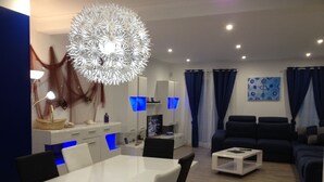 Un salon moderne avec une table à manger blanche, des chaises noires, un canapé bleu et un grand luminaire décoratif.
