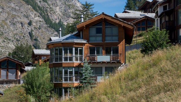 A mountain lodge with a wooden exterior, large windows, and a balcony. - Superior apartment with stunning Views of Matterhorn.  1 free return taxi ride (Zermatt)
