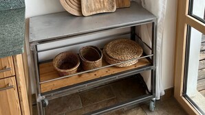 A kitchen area with a metal cart holding wooden cutting boards and baskets, and two wall-mounted paintings of a cup. - Superior apartment with stunning Views of Matterhorn.  1 free return taxi ride (Zermatt)