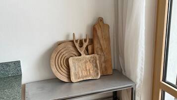 Eine Küchenzeile mit einem Metallwagen, der Holzschneidebretter und Körbe trägt, und zwei an der Wand hängende Bilder einer Tasse.