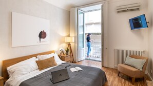 Een hotelkamer met een bed, een laptop, een boek, een lamp, een stoel en een televisie.