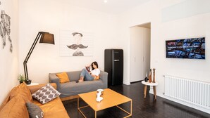 Een moderne woonkamer met een bank, salontafel en een aan de muur bevestigde televisie.
