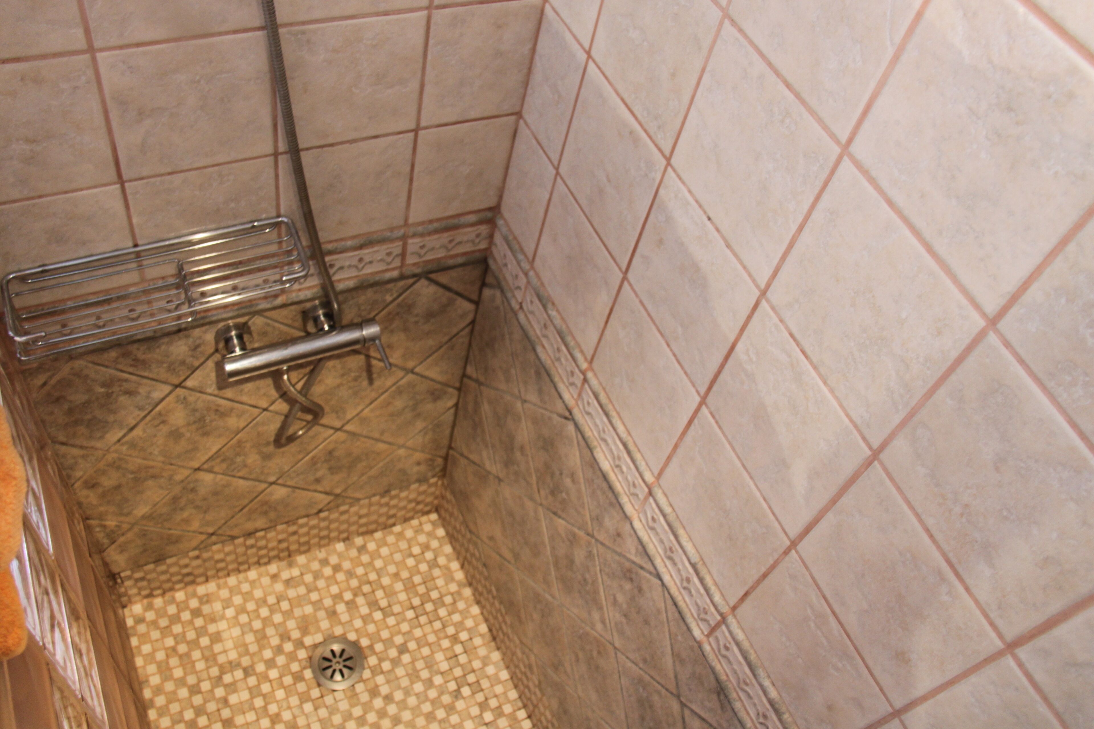 Un baño pequeño con azulejos, zona de ducha, un estante metálico y desagüe.