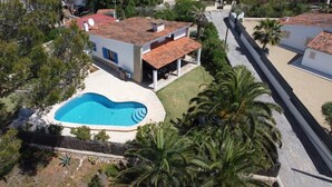 A residential area with a swimming pool, houses with red-tiled roofs, and palm trees. - Villa-Chalet with private pool, POOLSIDE BARBECUE (Manacor)