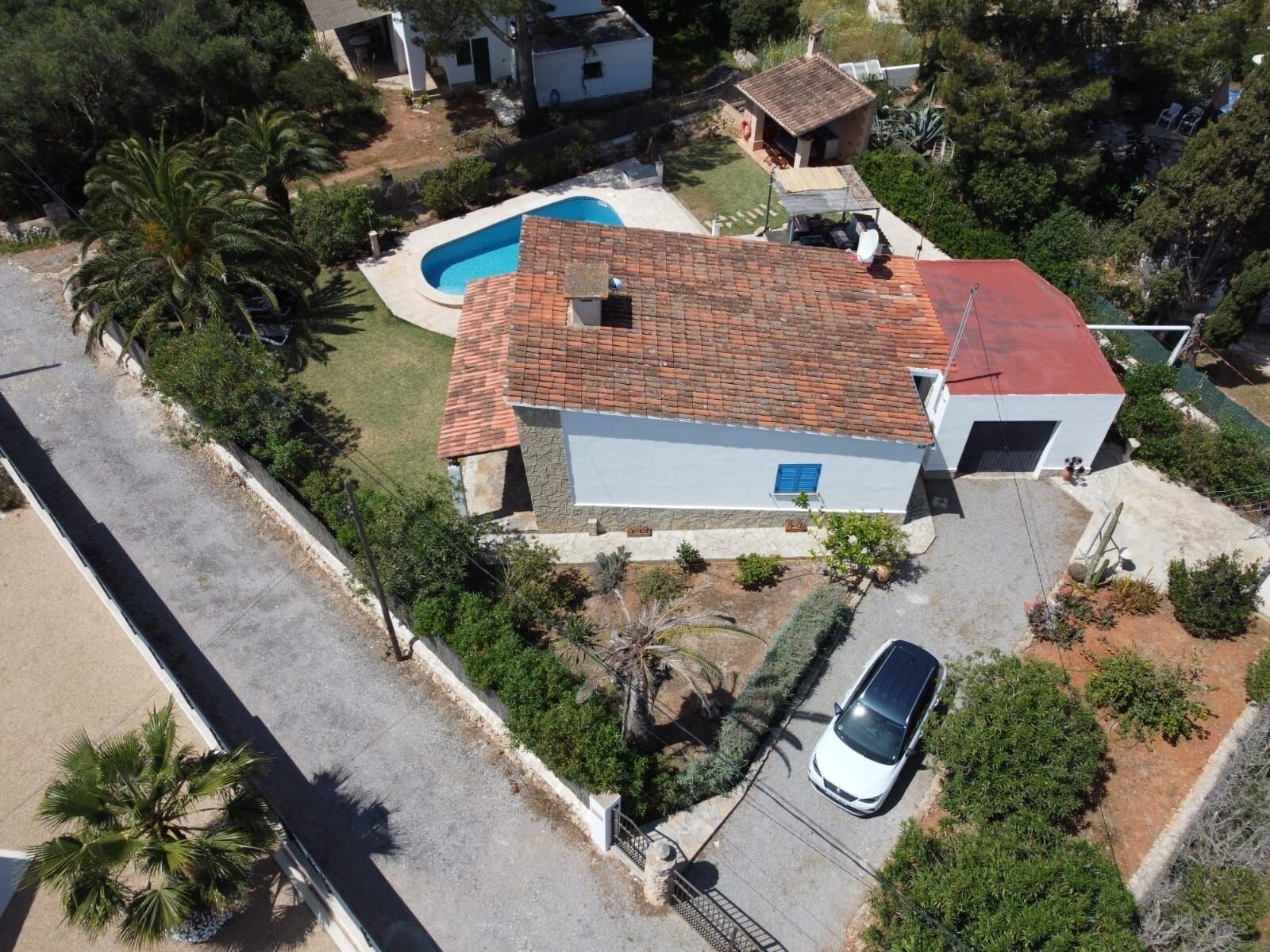 A residential property with a swimming pool, a car parked in the driveway, and a red-tiled roof.