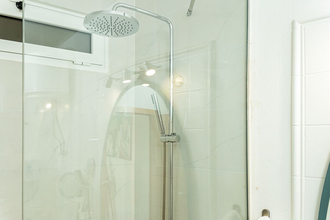 Een douchecabine met glazen wanden, een handdouche en een kraan op de muur.
