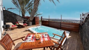 Een terras op het dak met een jacuzzi, houten terras, stenen muur en uitzicht op het landschap.