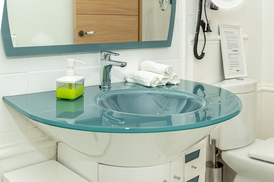 A bathroom with a glass sink, a mirror, a white toilet, and a towel rack.