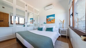 Een slaapkamer met een bed, nachtkastje, spiegel, schilderij en raam.