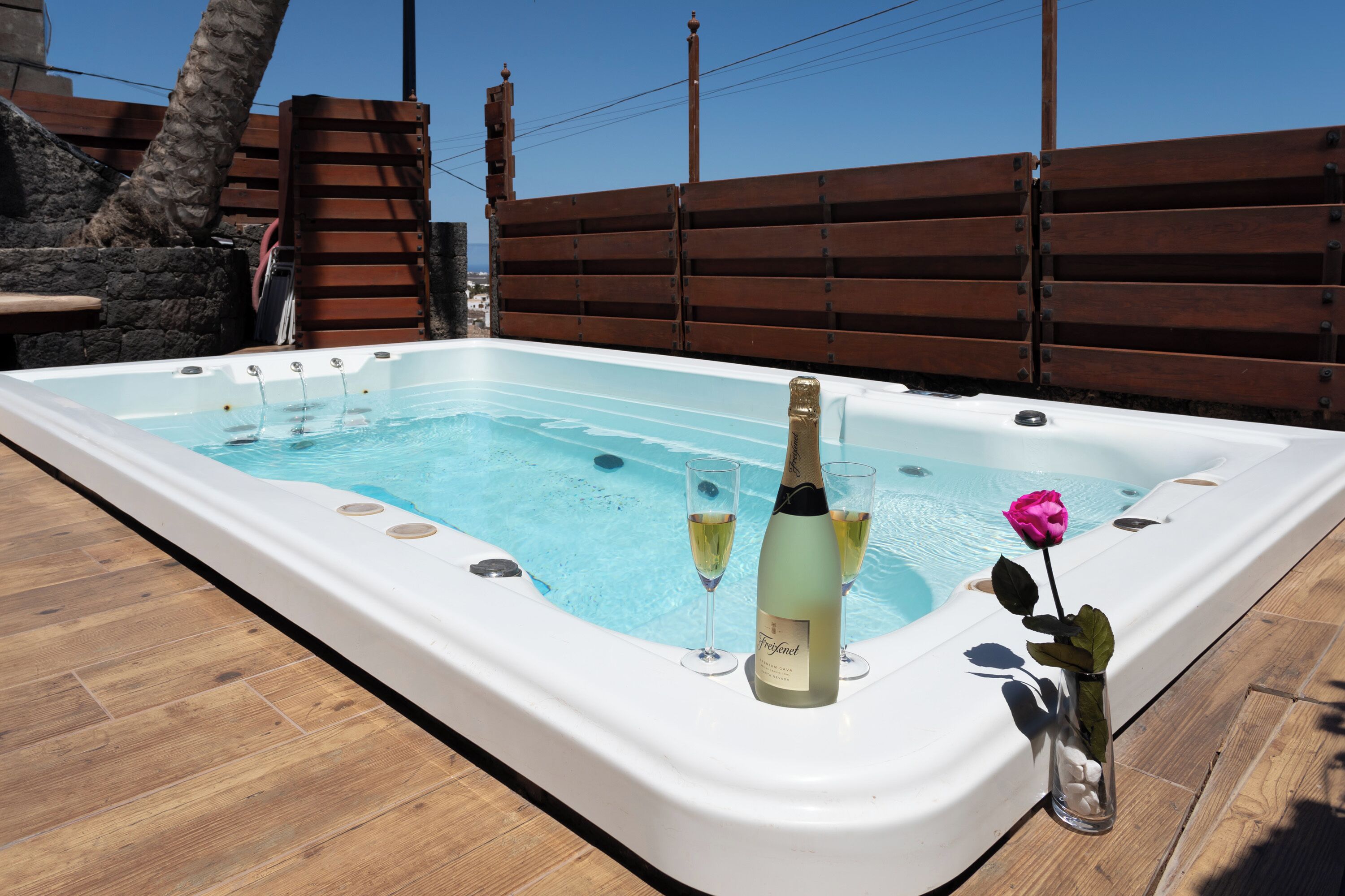 A hot tub with a wooden deck, a rose, and two champagne glasses.