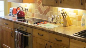Una cocina con armarios de madera, un lavamanos de acero inoxidable, una tetera, un tostador y un bloque de cuchillos.