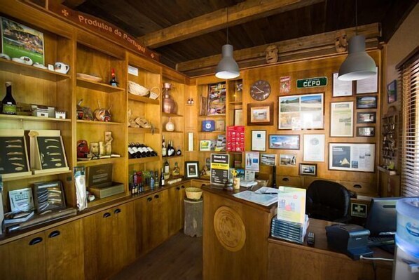 A rustic interior with wooden shelves displaying various items, a wooden counter with a computer, and framed pictures on the walls.