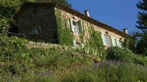 A stone house with a tiled roof, surrounded by lush greenery and purple flowers. - House with character in the Countryside/mountain - 6 bedrooms - Cevennes/Gard (Soudorgues)