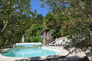 Una piscina con lettini e ombrelloni, circondata da vegetazione e un muro in pietra.