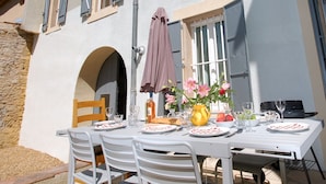 Une table dressée pour un repas en plein air, avec vue sur un bâtiment doté de nombreuses fenêtres et d’une arche.