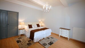 Une chambre à coucher comprenant un lit, des tables de chevet, une commode, un lustre et un radiateur.