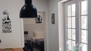 A modern hotel room with a black pendant light, a bed with white bedding, a small table with a woven basket, and a door leading to a balcony. - Small and lovelly villa, in the center of Peniche, in a quiet zone, for 5 persons (Peniche)