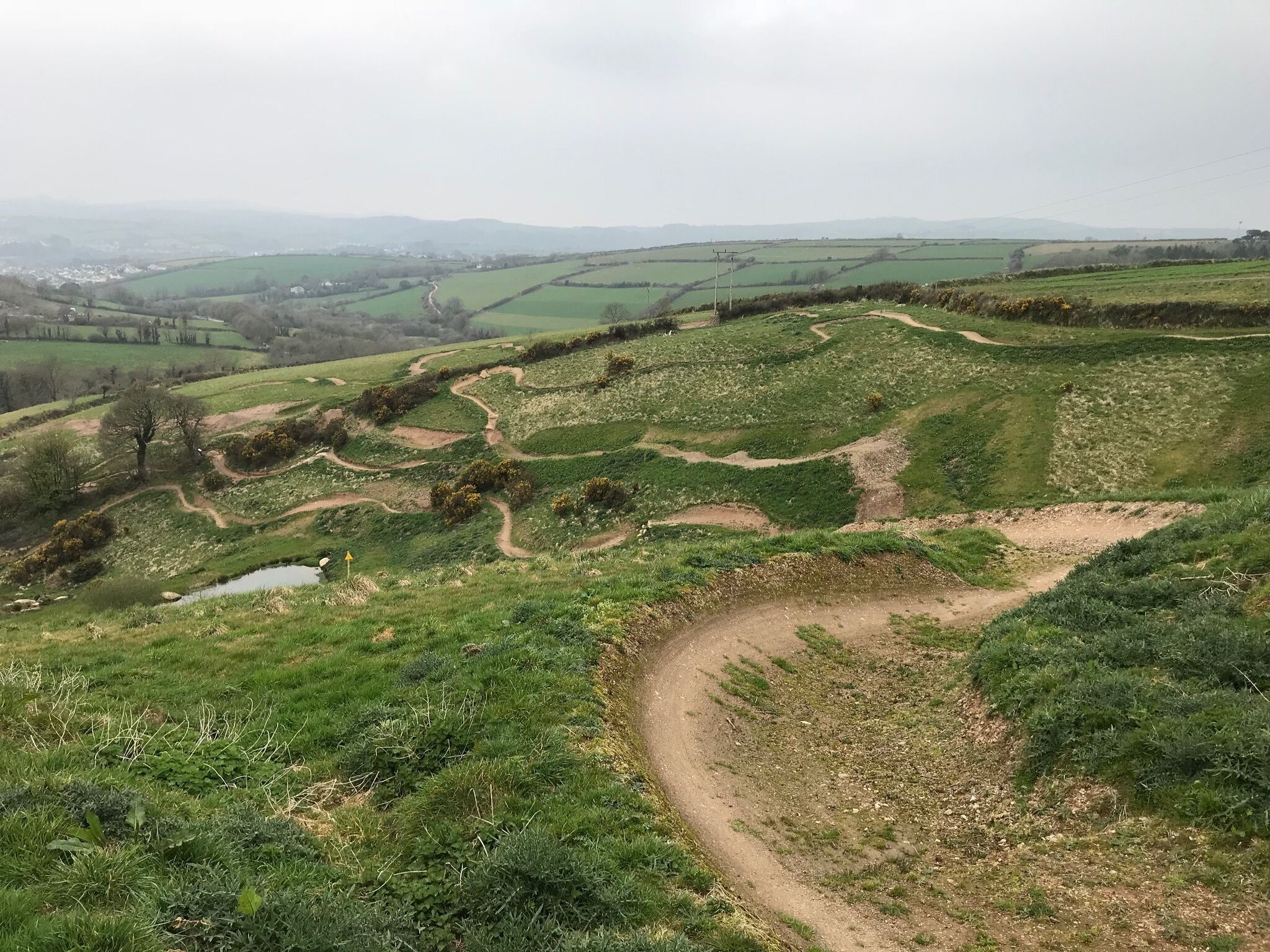 A rural landscape with rolling green fields, a winding dirt path, and a small pond.