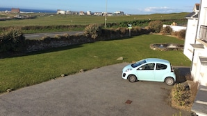 A light blue car parked in a driveway with a view of a grassy area and buildings in the distance.