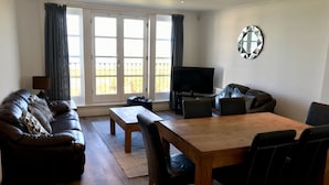 A living room with a sofa, a coffee table, a TV, and a dining table with chairs.