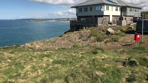 A coastal house with a large deck overlooking the sea, a stone foundation, and a modern design.
