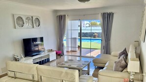 Ein Wohnzimmer mit einer Couch, einem Fernseher und Blick auf einen Pool.