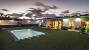 Ein modernes Haus mit Swimmingpool, überdachter Terrasse und gepflegtem Rasen.