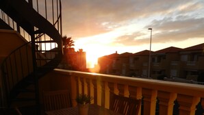 A balcony with a wooden table and chairs, a potted plant, and a spiral staircase. - Wonderful apartment in Bahía del Duque - Pool, 2 Terraces, Wifi ... (Costa Adeje)