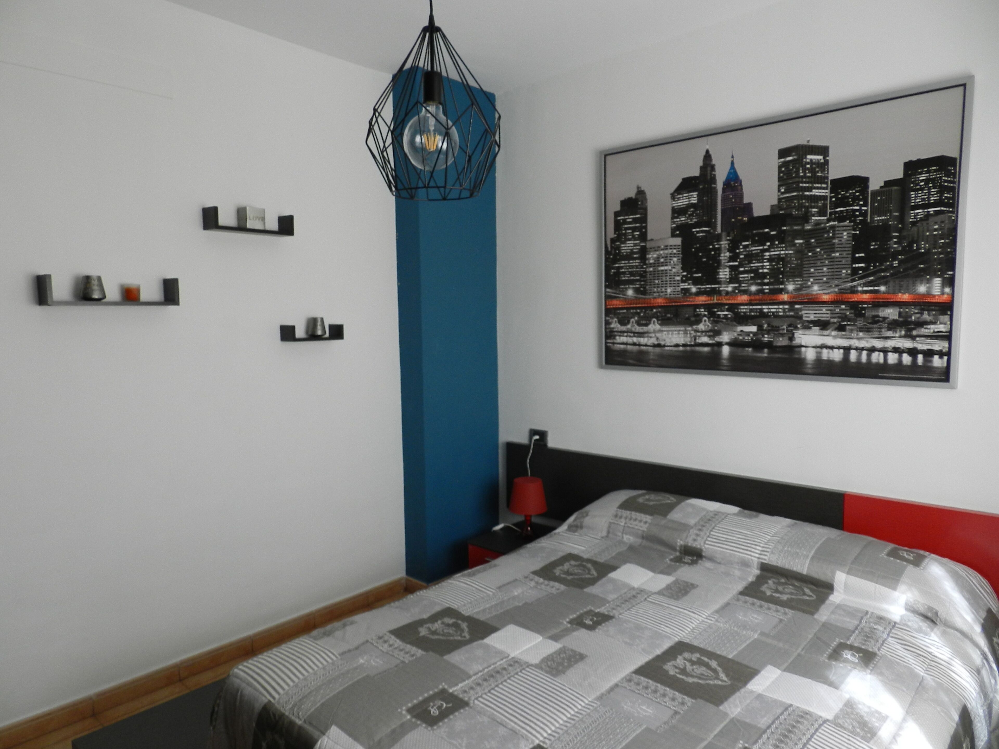 Un dormitorio moderno con vista a un paisaje urbano, una lámpara de diseño geométrico y una mesita de noche ordenada.