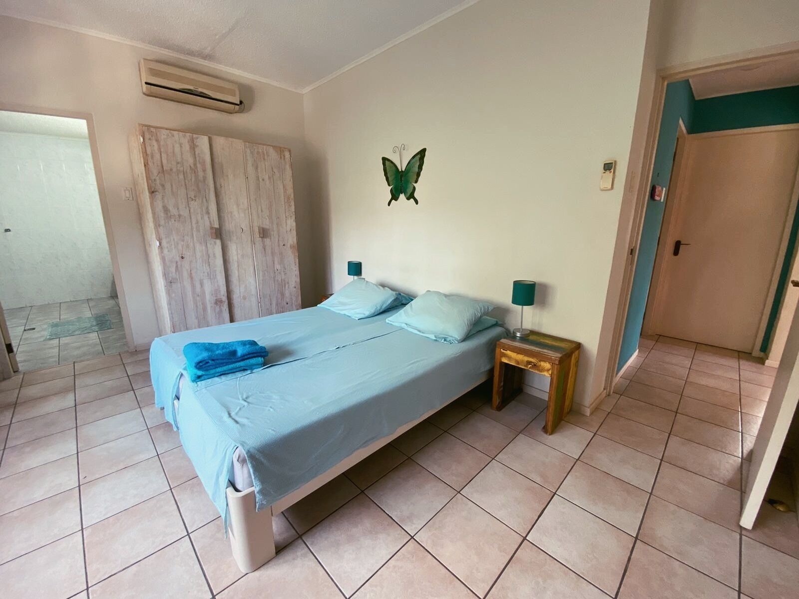 Un dormitorio con cama, almohadas, mesita de noche, una decoración de mariposa en la pared y un equipo de aire acondicionado.
