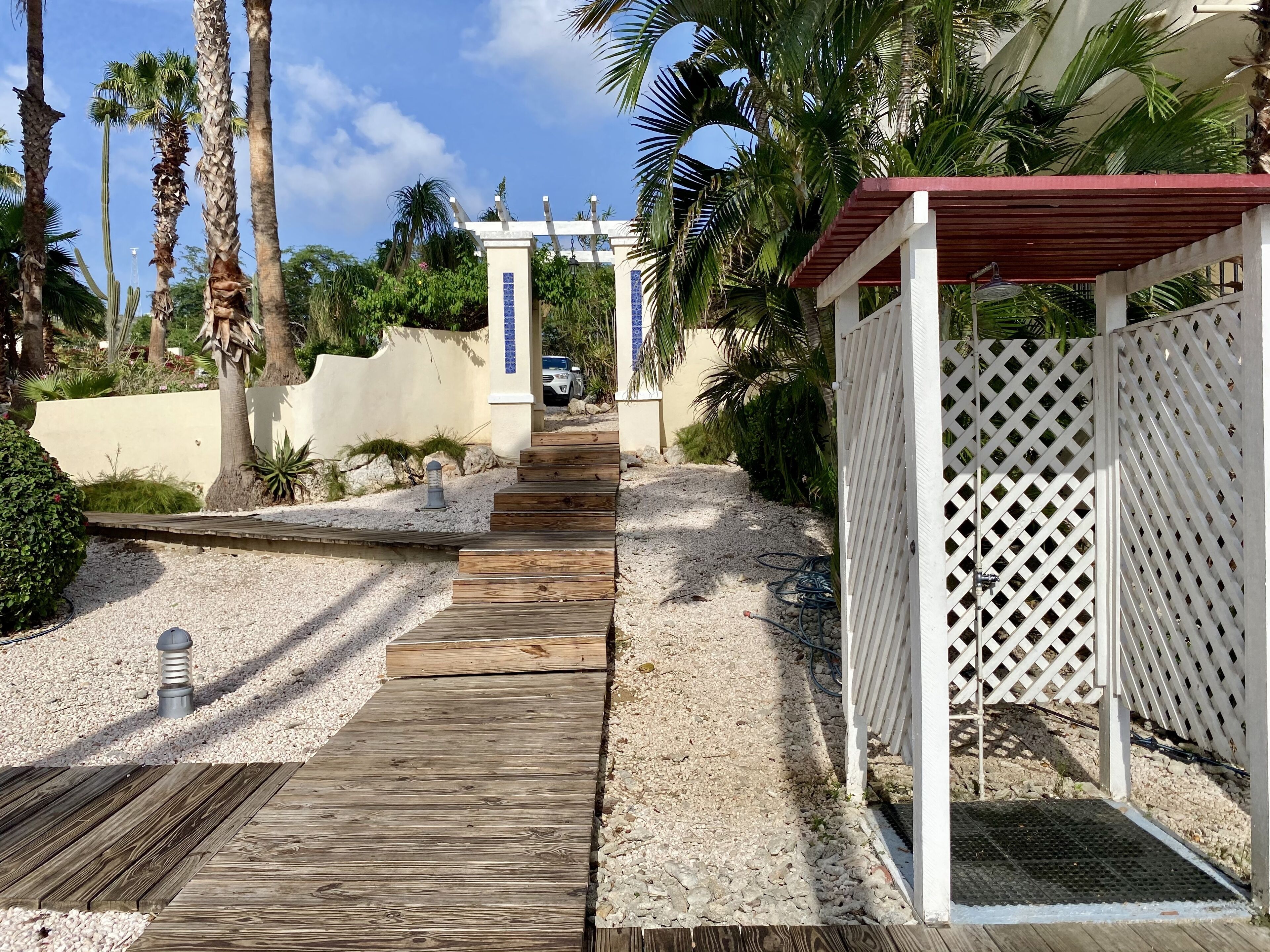 A wooden pathway leading to a covered area with a white lattice fence.