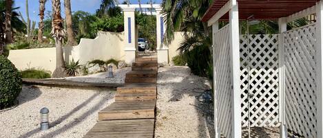 A wooden pathway leading to a covered area with a white lattice fence.