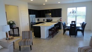 A modern kitchen with dark cabinets, a central island with stools, and a dining area with chairs.