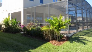 A house with a large glass-enclosed porch, surrounded by a well-maintained garden with various plants and flowers.