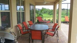 A covered patio with a grill, outdoor table, and chairs.