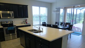 A modern kitchen with a large island, stainless steel appliances, and a dining area with a view.