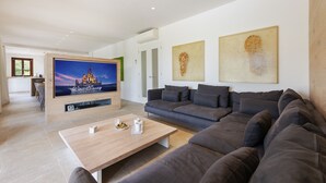 A modern living room with a large flat-screen TV, a grey sofa, a wooden coffee table, and two abstract paintings on the wall. - Villa Can Dala luxury in Port de Pollensa Sleeps 12 (Puerto Pollensa)