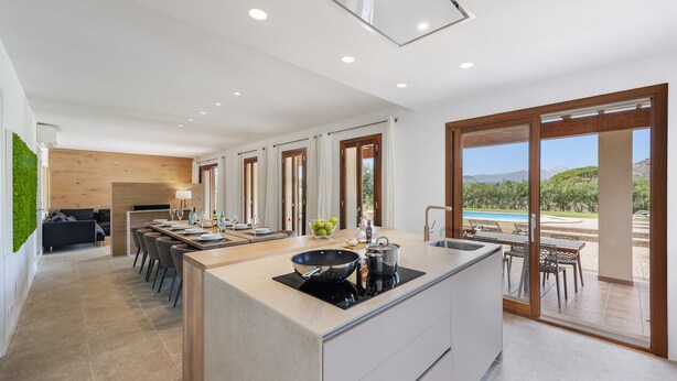 A modern kitchen with an island, dining area, and large sliding glass doors leading to a pool. - Villa Can Dala luxury in Port de Pollensa Sleeps 12 (Puerto Pollensa)