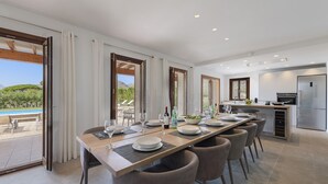 A modern dining area with a long table, chairs, and a view of a pool and mountains. - Villa Can Dala luxury in Port de Pollensa Sleeps 12 (Puerto Pollensa)