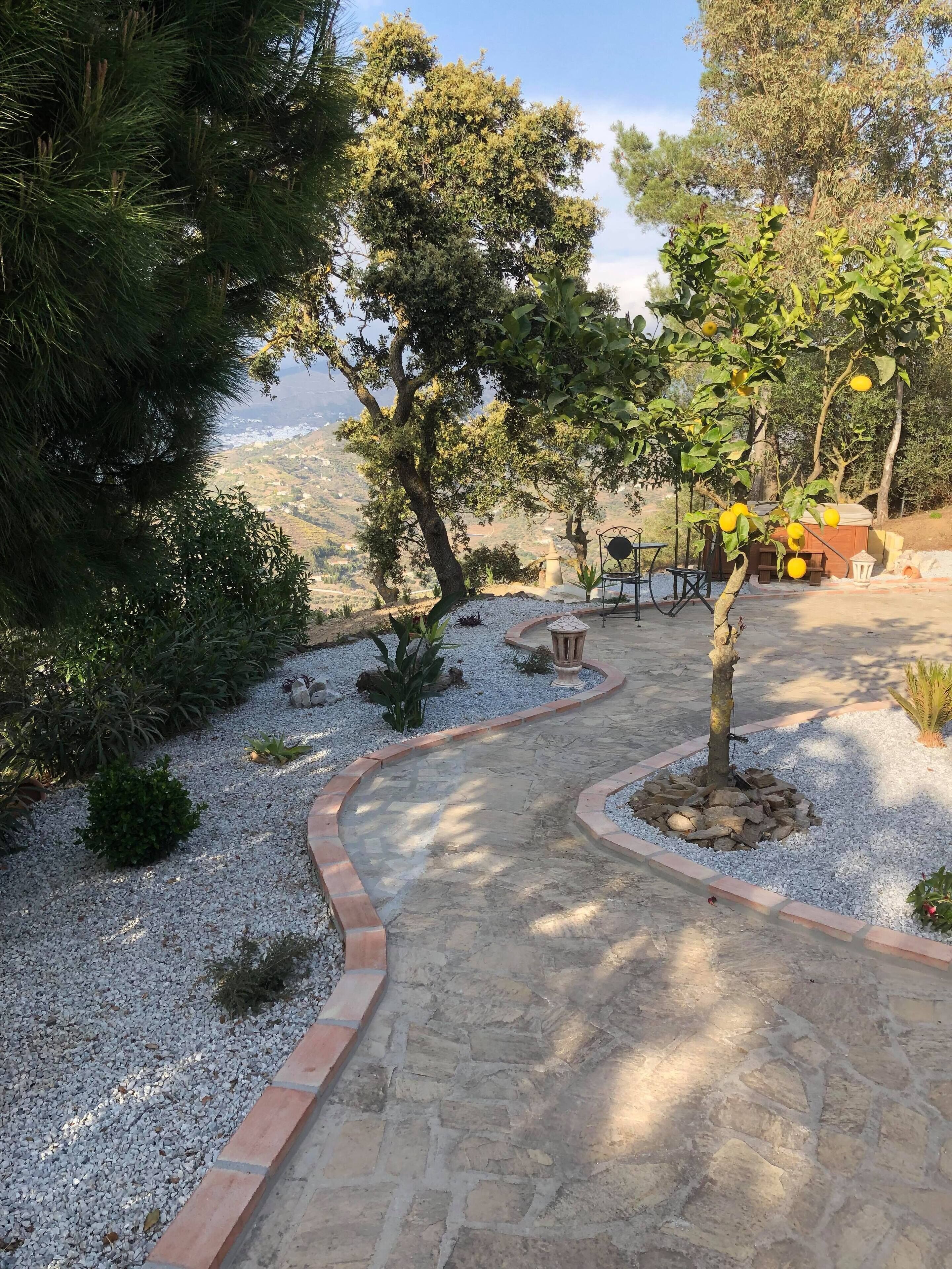 Un sentiero in pietra che si snoda attraverso un giardino curato, con alberi e vista su un paesaggio lontano.