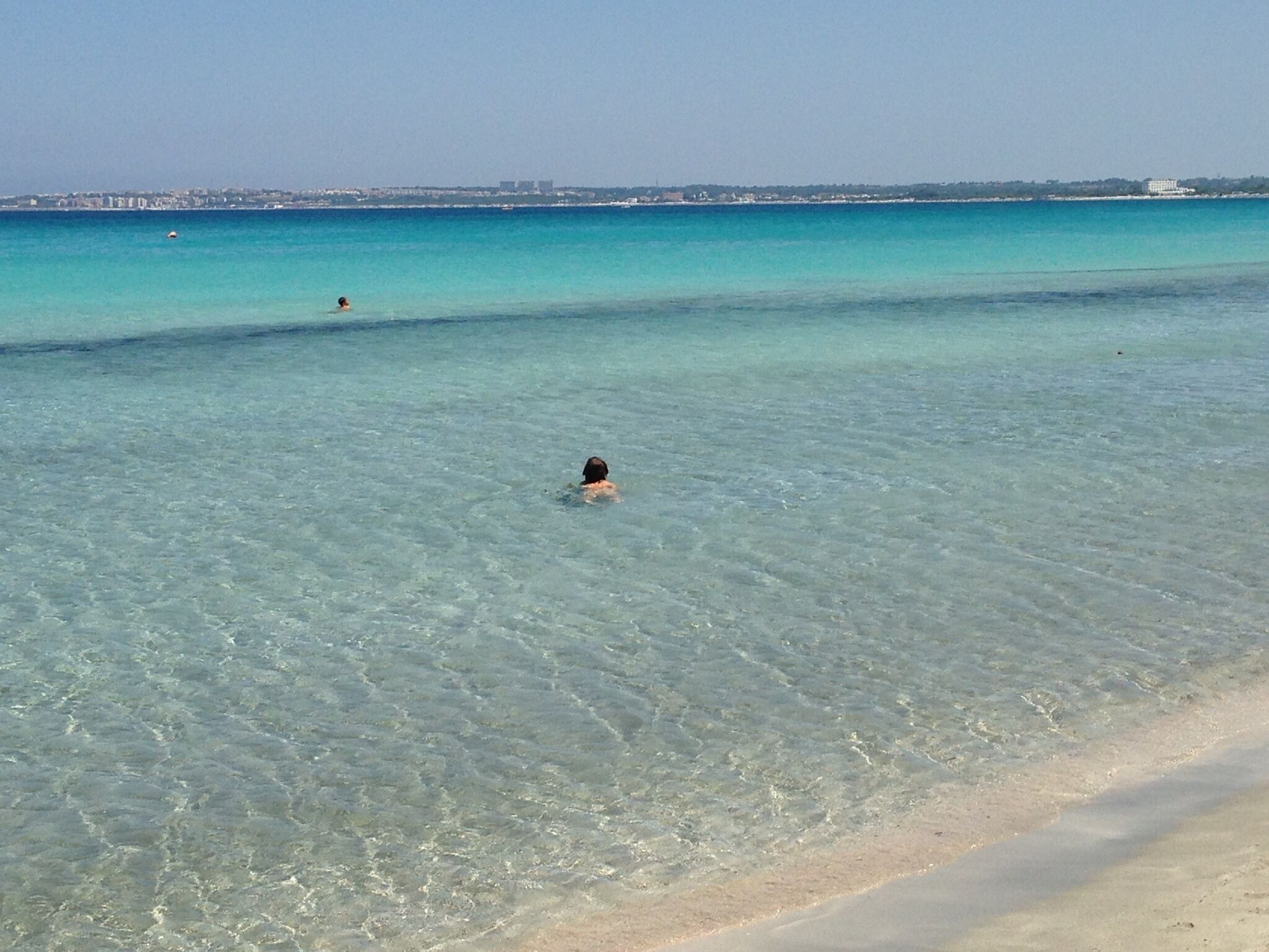 A beach with clear turquoise water and a person swimming.