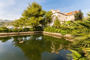 A serene courtyard with a reflective pond, surrounded by lush greenery and a historic building with a red-tiled roof. - Heritage Dvori with garden, free parking next to sea beautiful location  (Dubrovnik)