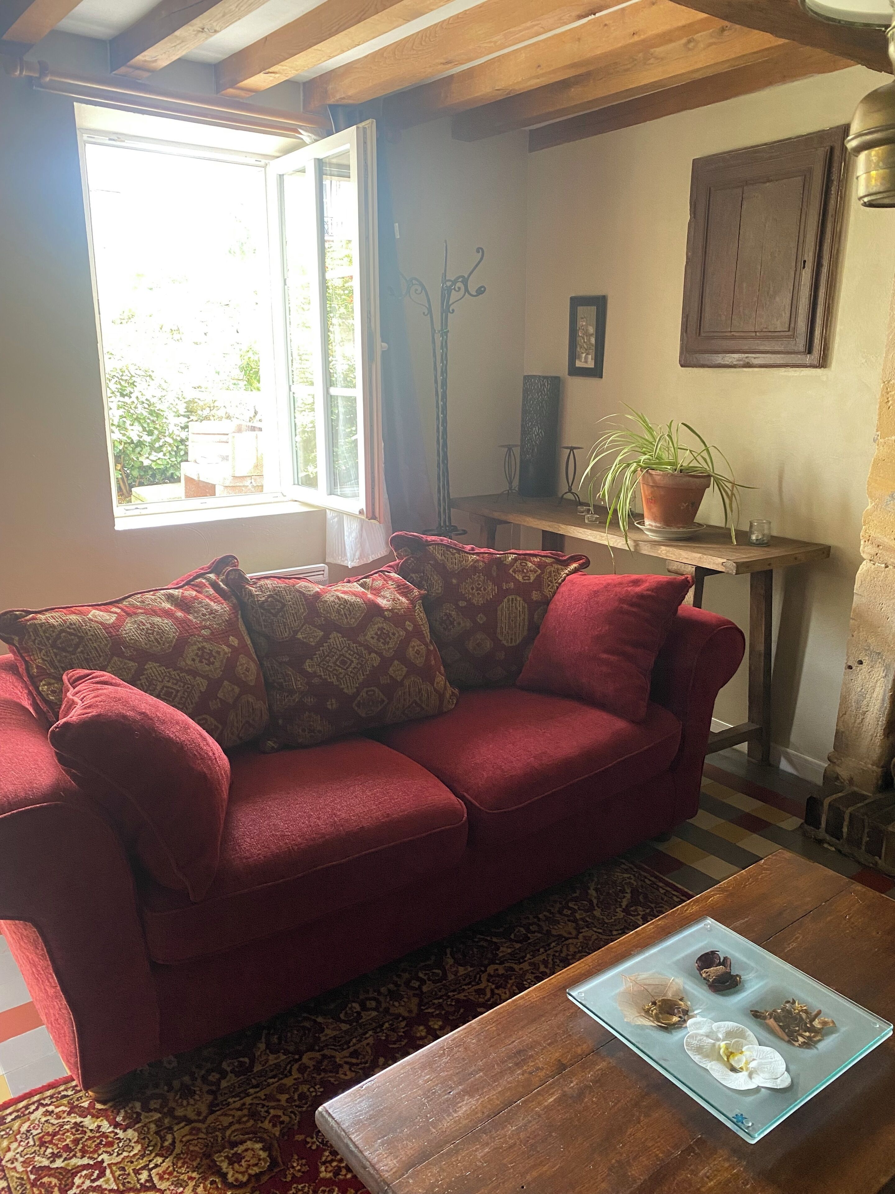 A cozy room with a red sofa, a wooden table with a glass display, and a window with a view of greenery.