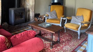 A cozy living room with exposed wooden beams, a fireplace, a yellow armchair, a red sofa, and a patterned rug. - Karen House 5mn Omaha Beach DDay in Aure-sur-mer (Aure sur Mer)
