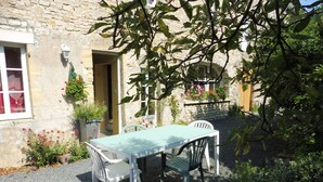 A rustic stone building with a small garden patio featuring a table and chairs. - Karen House 5mn Omaha Beach DDay in Aure-sur-mer (Aure sur Mer)