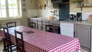 A kitchen with a red and white checkered tablecloth, wooden chairs, a tiled floor, and a window with a view of trees. - Karen House 5mn Omaha Beach DDay in Aure-sur-mer (Aure sur Mer)